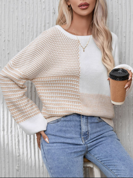 A woman wearing a beige and white long sleeve sweater with a round neckline, paired with blue jeans.